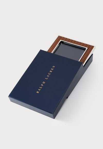 Brązowa pleciona ramka na zdjęcia ze skóry z srebrnym akcentem, umieszczona w granatowym pudełku z złotym napisem "RALPH LAUREN" na górze.