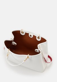 Witte totebag met een gestructureerde buitenkant, gouden hardware en een bruine binnenkant. Voorzien van een binnenvak en een contrasterende band met rood-witte details.