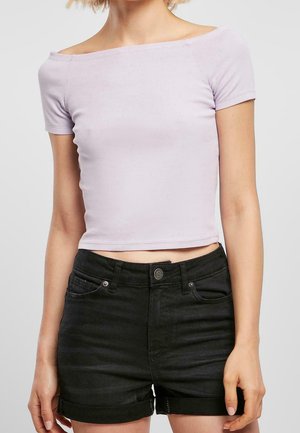 Kobieta ubrana w jasnofioletowy, odkrywający ramiona, krótki top oraz czarne, wysokowalne dżinsowe szorty z podwiniętymi brzegami.