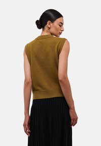 Top sans manches en maille moutarde avec un ourlet côtelé et un col, associé à une jupe noire plissée. Texture lisse et design ajusté.