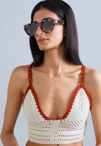 Crochet bralette in cream and burnt orange with triangular cups, detailed stitching, and thin straps. Accessories include oversized tortoiseshell sunglasses.