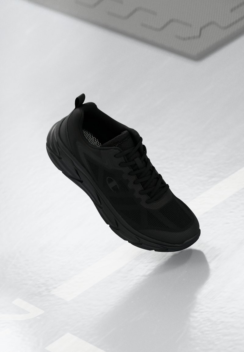 Black athletic shoe featuring a mesh upper, textured sole, and a pull tab at the back. The design is streamlined with subtle branding.