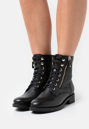 Černé kotníkové boty z kůže s texturovaným povrchem, vybavené zlatými kovovými prvky, šněrováním vpředu a bočním zipem pro snadné nazouvání. Nízký blokový podpatek.