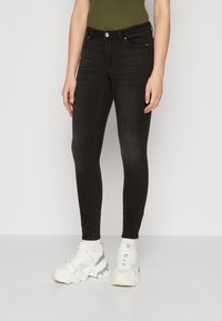 Černé skinny džíny z denimu, s pětivreckovým designem a štíhlým střihem. Kombinované s robustními bílými teniskami a žebrovaným zeleným topem.