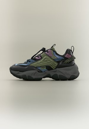 Zapatilla gruesa con paneles negros, verdes, azules y morados, suela gruesa, lengüeta para tirar y cordón elástico con cierre en un fondo neutro.