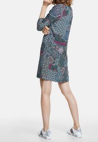 Robe à motifs en bleu sarcelle foncé avec des motifs circulaires rouges, roses et crème, associée à des baskets blanches avec des accents floraux noirs.