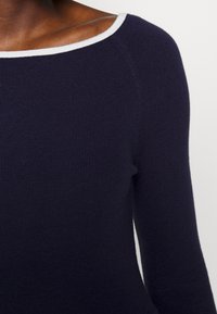 Close-up of a person wearing a navy blue ribbed knit sweater with a white trim around the wide neckline.