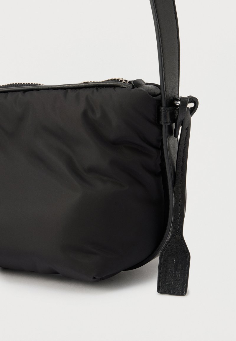 Sac bandoulière en nylon noir avec sangle en cuir et fermeture éclair, avec une étiquette en cuir attachée à la boucle de la sangle.