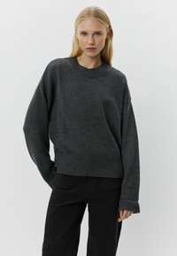 Maglione oversized grigio scuro con collo a girocollo e polsini a coste. Tessuto morbido e spalle scese; abbinato a pantaloni neri.