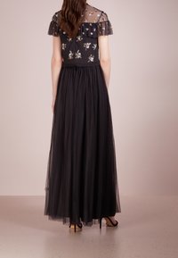 Robe de soirée noire avec un corsage transparent brodé de fleurs, des manches volantes et une jupe en tulle fluide avec une texture à pois.