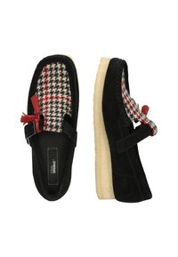 Zwarte suède schoenen met een geruite wol bovenkant, voorzien van een rode kwast en een verstelbare riem. Beige rubberen zool, ronde vorm.