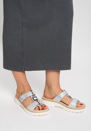 Füße in silbernen Plateausandalen mit dekorativen Schnallen, rot lackierten Zehennägeln und einem dunkelgrauen Midirock, der von der Mitte der Waden abwärts sichtbar ist.