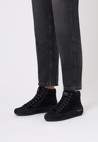 Sneaker alte nere realizzate in suede testurizzato, dotate di una cerniera laterale e chiusura con lacci, abbinate a jeans neri a sigaretta.