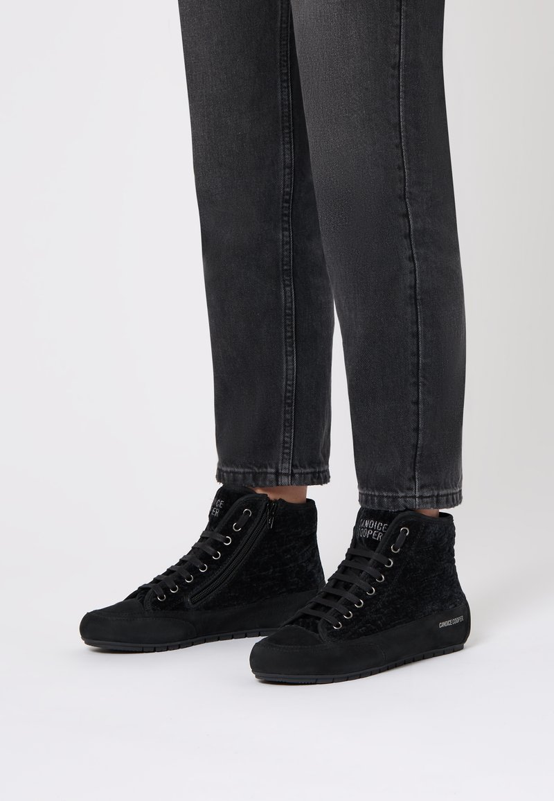 Sneaker alte nere realizzate in suede testurizzato, dotate di una cerniera laterale e chiusura con lacci, abbinate a jeans neri a sigaretta.