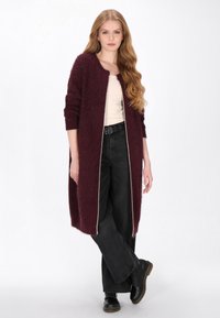 Burgundowy długi kardigan o fakturowanym splocie, z otwartym przodem i kontrastowymi białymi wykończeniami. Połączony z czarnymi spodniami typu wide-leg i czarnymi botkami.