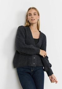 Cardigan grigio lavorato a maglia con scollatura a V, texture a coste e tre grandi bottoni. Presenta maniche lunghe e una vestibilità rilassata.