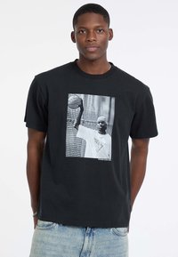 T-shirt en coton noir avec un graphique en façade d'un joueur de basketball. Conception à col rond avec des manches courtes et coupe décontractée.