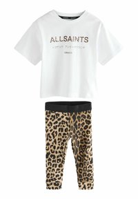 Biała bawełniana koszulka z logo "ALLSAINTS" w wężowy wzór, zestawiona z czarnymi legginsami w wężowy wzór, mającymi czarną, gładką gumkę w pasie.