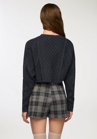 Maglione corto navy con texture a trecce, abbinato a pantaloni corti a vita alta a quadri in tonalità neutre. Calze alti fino alla coscia completano il look.