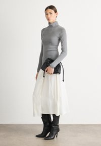 Grauer gerippter Rollkragenpullover, weißer Midirock, schwarze Tasche mit Kordelzug und kniehohe schwarze Stiefel mit Absatz und spitzer Zehenform.