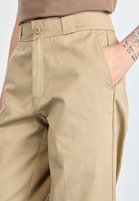 Pantaloni in cotone beige con taglio dritto, dotati di chiusura con un solo bottone, tasche frontali e superficie liscia.