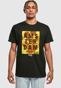 Melns kokvilnas T krekls ar krāsainu grafiku, kurā ir teksts "AMSTERDAM" un van Goga dizaini, piemērots ikdienas valkāšanai.