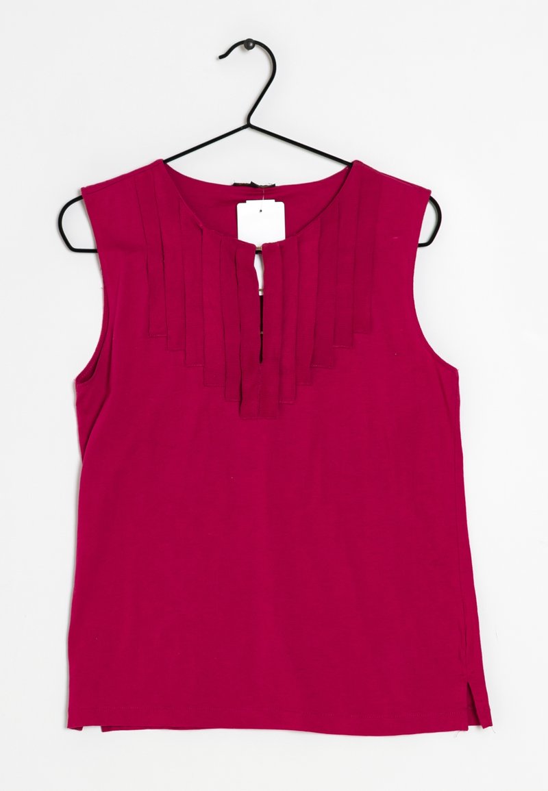 Haut sans manches fuchsia avec un col plissé, présentant une fente à l'avant et une étiquette attachée, fabriqué en tissu doux. Suspendu à un crochet noir.