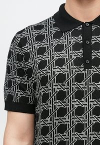 Čierno-biele pruhované polo tričko s geometrickým vzorom, krátkymi rukávmi, čiernym golierom a trojicou gombíkov na prednom diele.