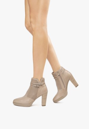 Bottes chelsea beiges avec un panneau en maille texturée, une fermeture éclair sur le côté et un talon empilé. Dotées d'une sangle avec une boucle en argent.