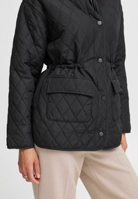 Schwarze, gesteppte Jacke mit einem elastischen Bund und zwei Fronttaschen, ausgestattet mit einem Knopfverschluss und einem strukturierten, gepolsterten Design.