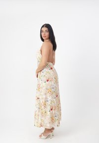Robe maxi florale avec un col halter, design dos nu, couleurs pastel douces et tissu fluide. Assortie avec des sandales à talons hauts et lanières.
