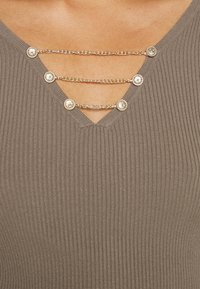 Gerippter taupefarbener Top mit V-Ausschnitt und drei silbernen Ketten mit runden Verzierungen entlang des Ausschnitts.