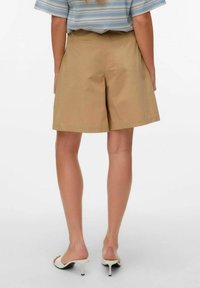 Beige katoenen shorts met een rechte snit, voorzien van zijzakken en een gladde textuur, gedragen met witte open teen-hakken.