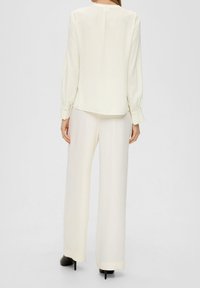 Blusa bianca con maniche lunghe e scollatura rotonda, abbinata a pantaloni a gamba larga. Tessuto morbido e leggero con un leggero lucido.