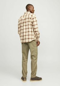Beige en bruine geruite flanellen overhemd met lange mouwen en knopenmanchetten, gecombineerd met groene cargobroek met zijzakken.