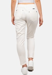 Pantalons blancs ajustés avec une taille élastique, des poches arrière et une texture lisse. Associés à des baskets blanches.