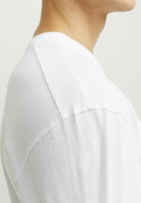 Balta trumpa rankovė t-shirt marškiniai, pasižymintys lygiu medvilniniu audiniu, apvaliu iškirpimu ir kontrastingais pečių siūlais.