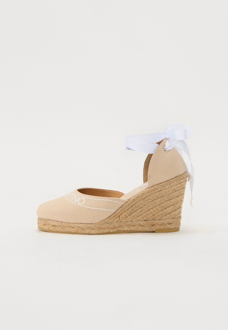 Wedge espadrille in beige canvas with white stitching and a ribbon tie at the ankle. Jute accent around the heel, rounded toe design.