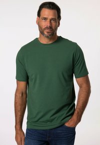T-shirt verde a maniche corte realizzato in tessuto morbido con scollo rotondo, caratterizzato da una texture liscia e una vestibilità classica. Indossato con jeans di denim.