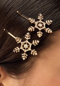 Guldtonade snöflingehårspennor dekorerade med klara rhinestones, med intrikata bladmönster och en glansig finish, fästa i mörkt hår.