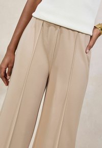 Beige wijde broek met plooien, gemaakt van een gladde, gestructureerde stof. Subtiele glans, met zijzakken en een elastische tailleband.