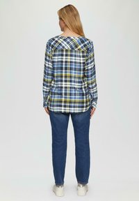 Blauwe en groene geruite lange mouwen blouse met een ronde zoom, gecombineerd met een donkere spijkerbroek en zilveren sneakers, gezien van de achterkant.
