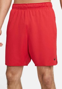 Uomo che indossa pantaloni corti da atletica rossi Nike con cintura elastica, mostrato dalla vita a metà coscia, su uno sfondo bianco.