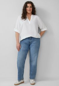 Witte linnen blouse met een V-hals en opgerolde mouwen, gecombineerd met lichtblauwe rechte jeans en witte sneakers met beige zolen.