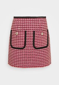 Jupe en tweed à motif pied-de-poule rouge et blanc avec bordure noire, deux poches avant soulignées de noir, et accents de boutons dorés.