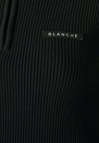 Pull noir à côtes avec un design à demi-zip et une petite étiquette rectangulaire portant le texte "BLANCHE." Tissu texturé avec des lignes verticales.