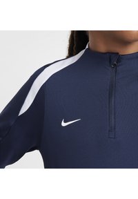 Marineblauw sporttop met een witte schouderstreep, halve rits kraag en het Nike-logo op de borst. Soepele stof met een aangesloten ontwerp.