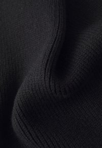 Tessuto a maglia nera con una superficie texturizzata e fine rigatura, che crea un aspetto morbido e caldo. Il materiale presenta una leggera elasticità.