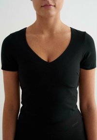 Top nero a maniche corte con scollatura a V. Il tessuto è liscio e aderente, evidenziando le curve del corpo.