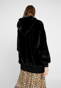 Czarna bluza z sztucznego futra w luźnym kroju, z oversized'owymi rękawami i zamkiem. Nosi się na sukience w kwiatowy wzór. Teksturowany, miękki materiał.